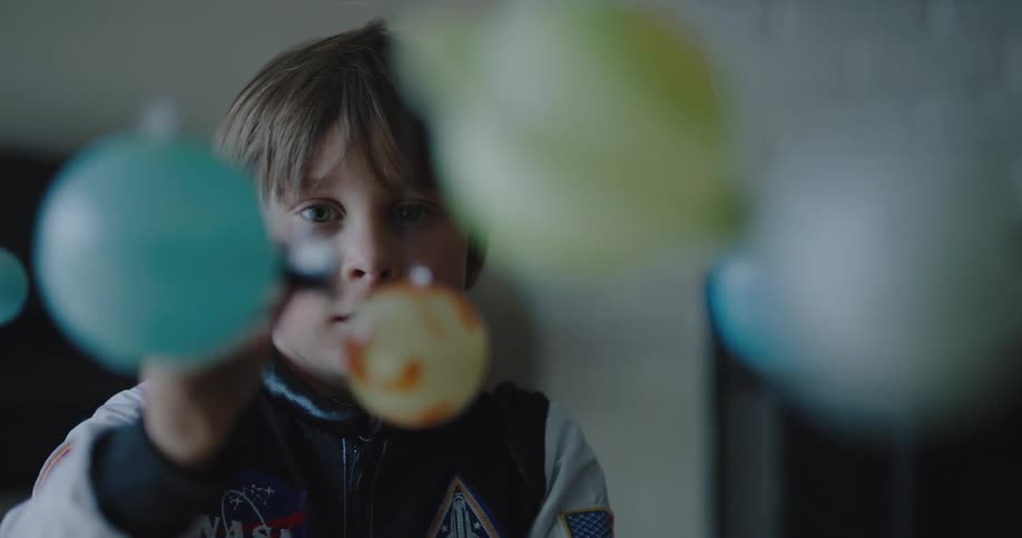 A little boy playing with a toy spaceship and planets inside his home