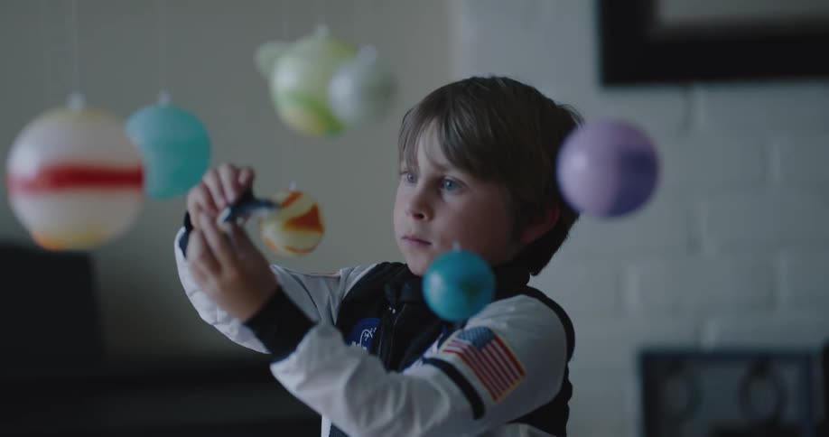 A young boy in an astronaut costume plays with a space shuttle toy and an orrery