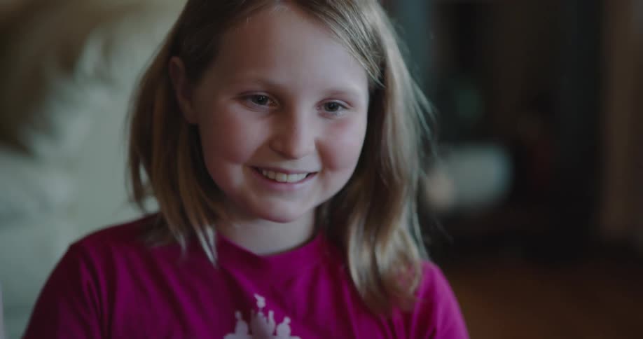 A young girl smiles while waving vigorously to someone else