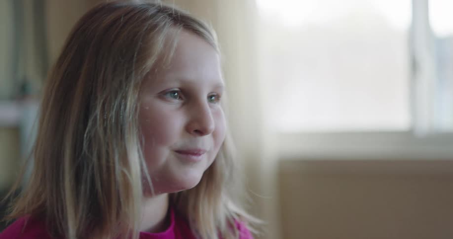 Blonde child with a long sleeve pink t shirt smiles and talks to a person in a room