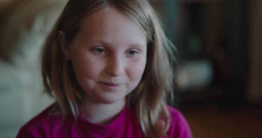 Blonde girl with a long sleeve pink t shirt speaks to a person and smiles in a room