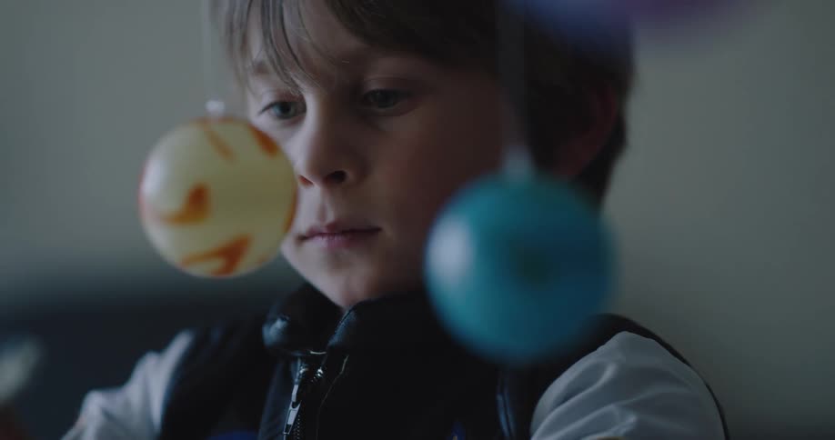 A young boy plays with a toy space shuttle and planets
