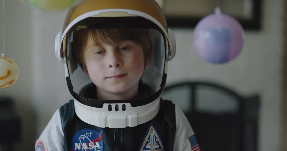 A little boy at home dressed in a space costume plays as planets hang down