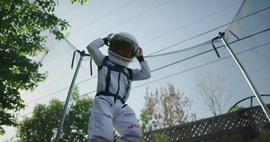 Child wearing astronaut costume bounce on trampoline in backyard