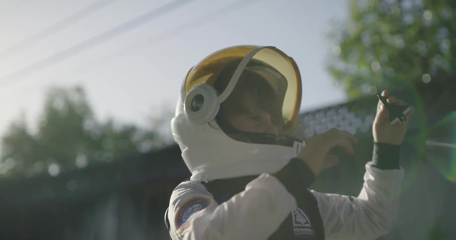 A little boy in a space suit plays with a toy spaceship in his back yard