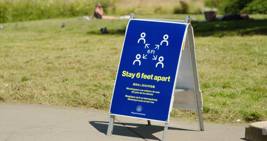 People relaxing on the grass in a park with a warning sign
