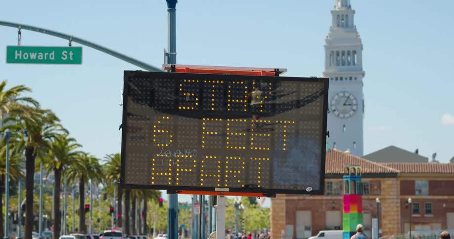 A digital sign with the city trees vehicles and people in the background