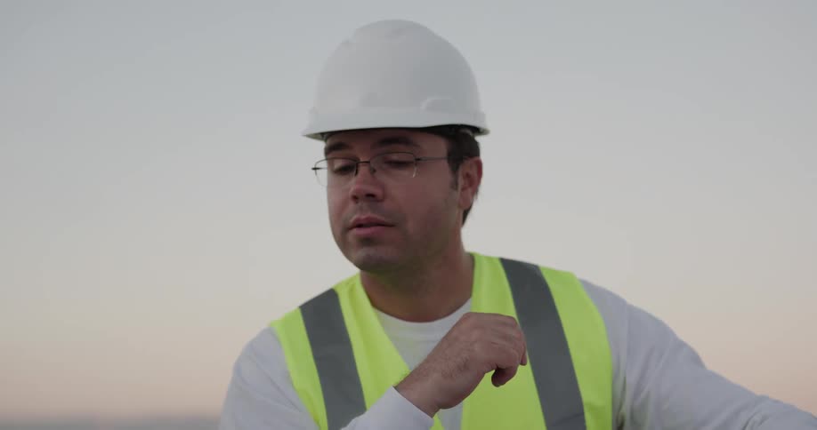 Two men on a construction site look at a blueprint and talk