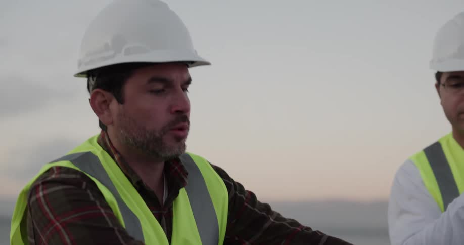Two men on a construction site look at blueprints