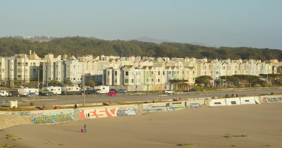 People relax on a beach located across the street from several apartment buildings that are separated from downtown by dense trees and hills