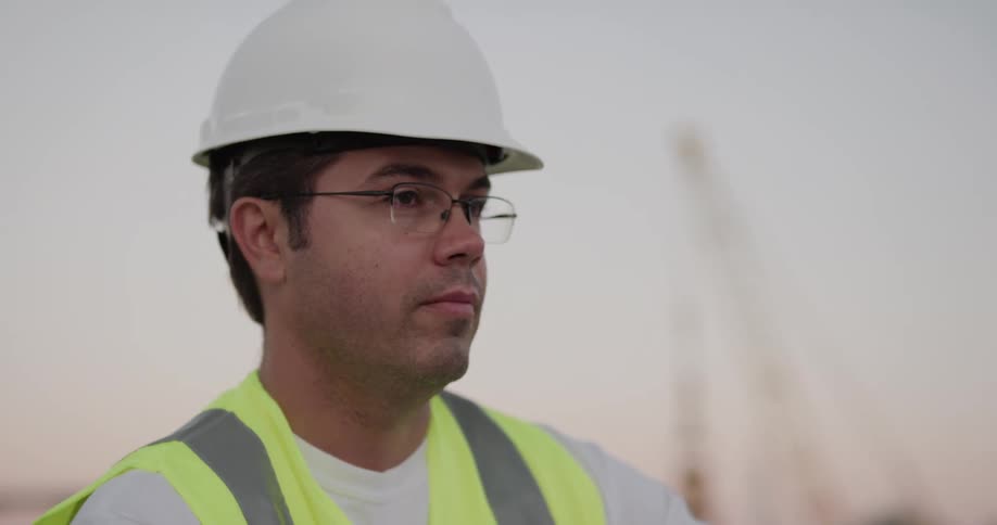 A construction worker discusses blueprints with a coworker in a dirt field
