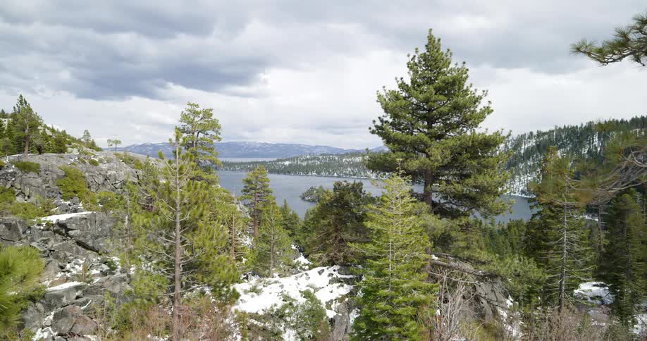 An evergreen forest in the snowy mountains and hills surrounding a lake under a cloudy sky