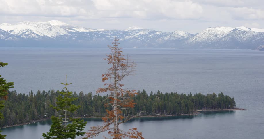 Snow covers mountain range surrounding lake on horizon as forest occupies peninsula