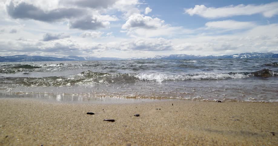 Small ocean waves break against coast with distant snowy mountains in the background