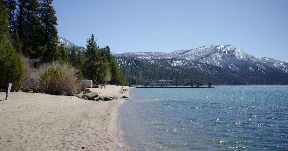 A person with a paddleboard walking on a lakeshore in the mountains