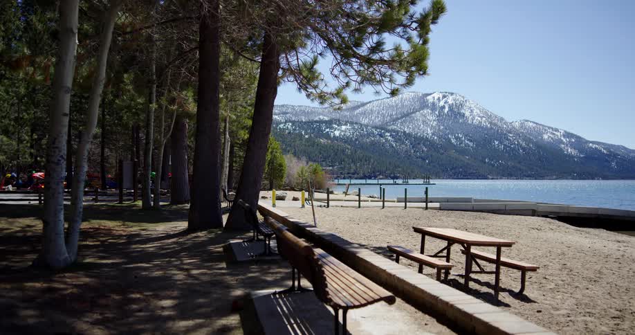 A picnic table and bench on a sandy lakeshore in the mountains