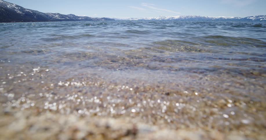 Small ocean waves break against coast with distant snowy mountains in the background
