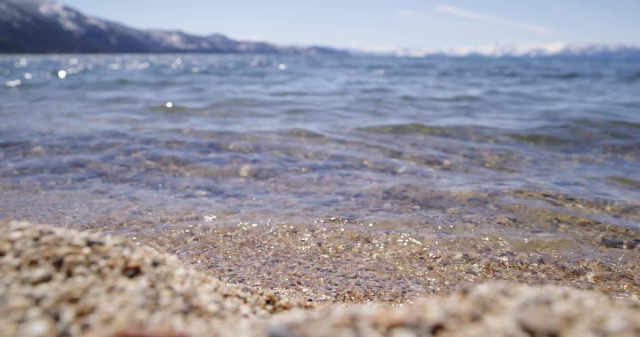 Small ocean waves break against coast with distant snowy mountains in the background
