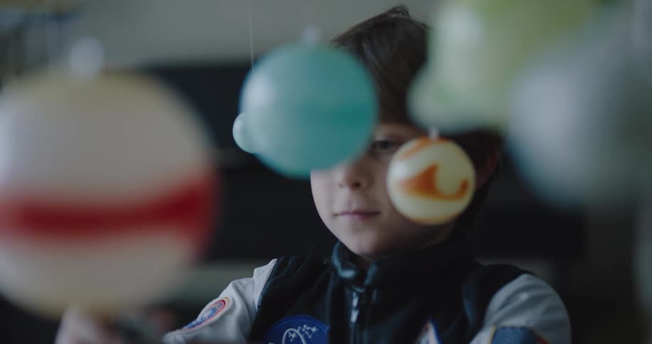 A little boy plays with a toy spaceship as play planets hang from the ceiling