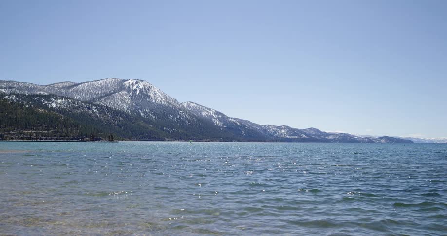 A lake shore with trees a mountain range the sky and clouds in the background