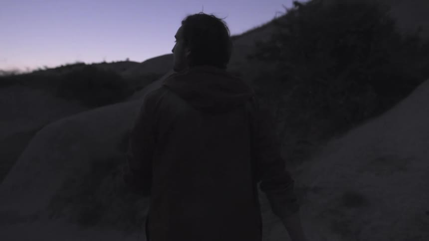 A man walks along the base of a rocky hill at dusk