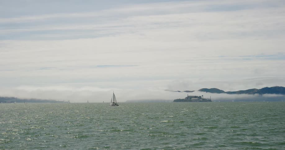 Dozens of sailboats sail far apart from each other in the ocean near mountains
