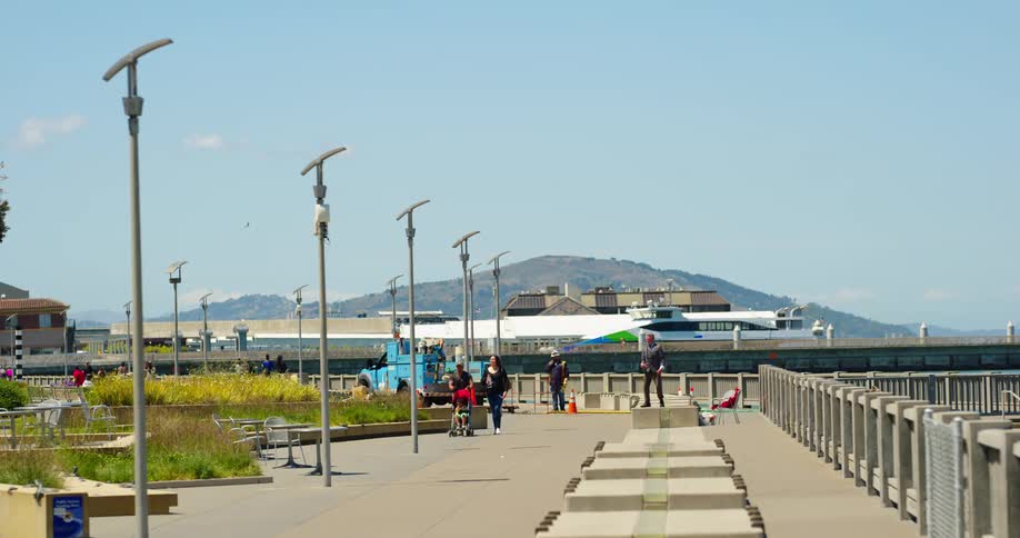 Mountain towers on horizon as pedestrians stroll along wide path bordered by railing and plant beds