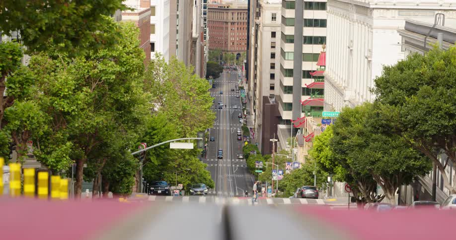 Pedestrian crosses intersection near base of steep hill while car drives up the hill