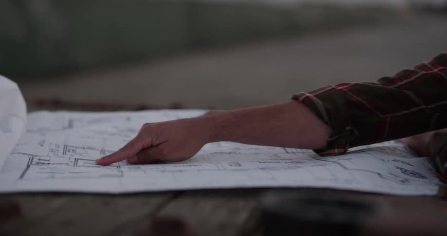 A construction worker discusses blueprints with another man as they stand in a ship yard