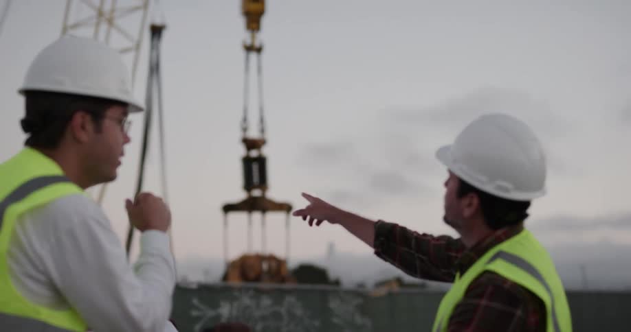 Two men on a construction site looks at blueprints and talk