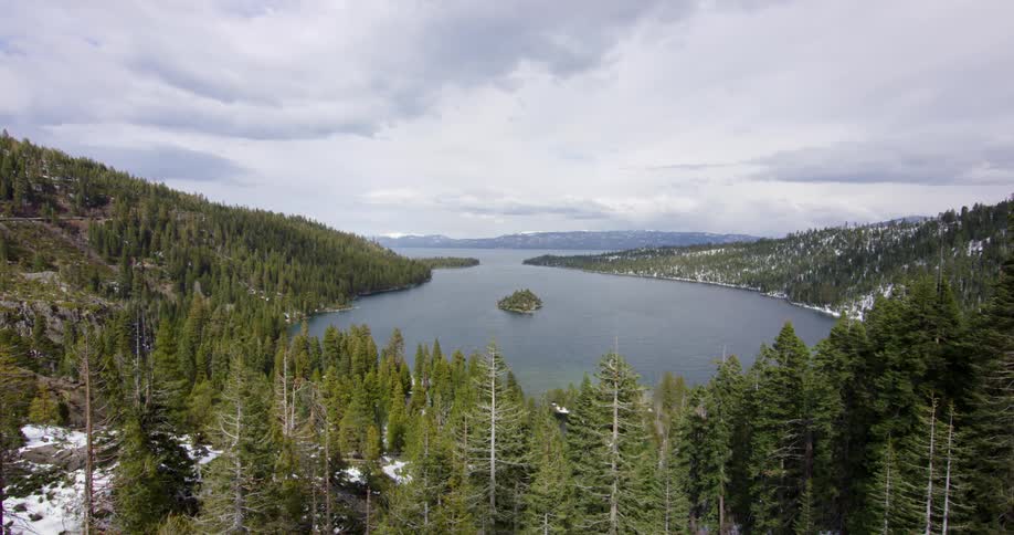 A lake surrounded by trees with a mountain range the sky and clouds in the background