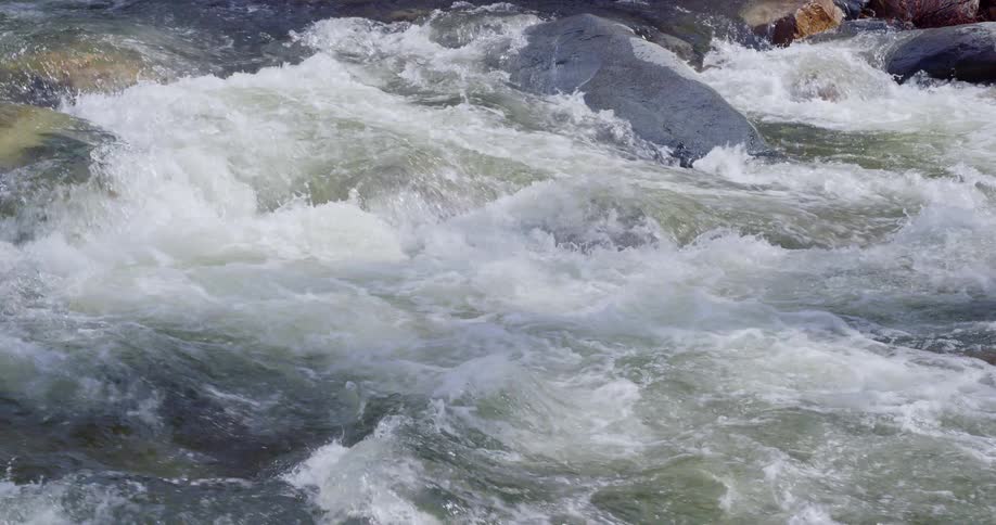 Water flows over large rocks into white water rapids