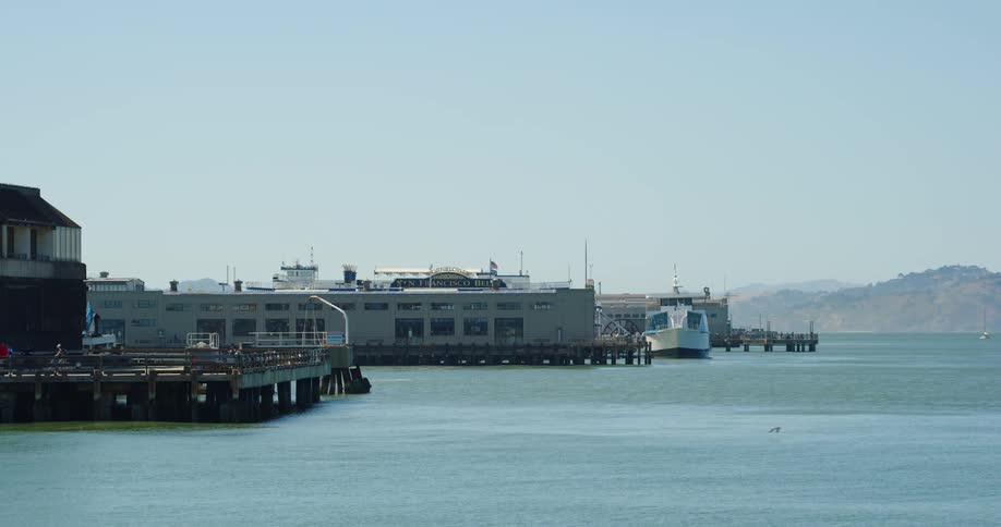 A coast with a pier and buildings with a mountain range and the sky in the background