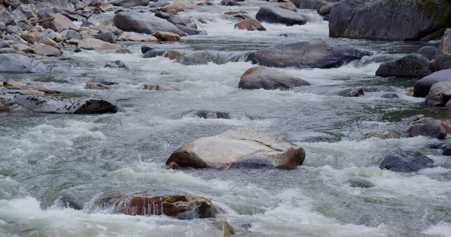 Water rushes over large boulders in a narrow river