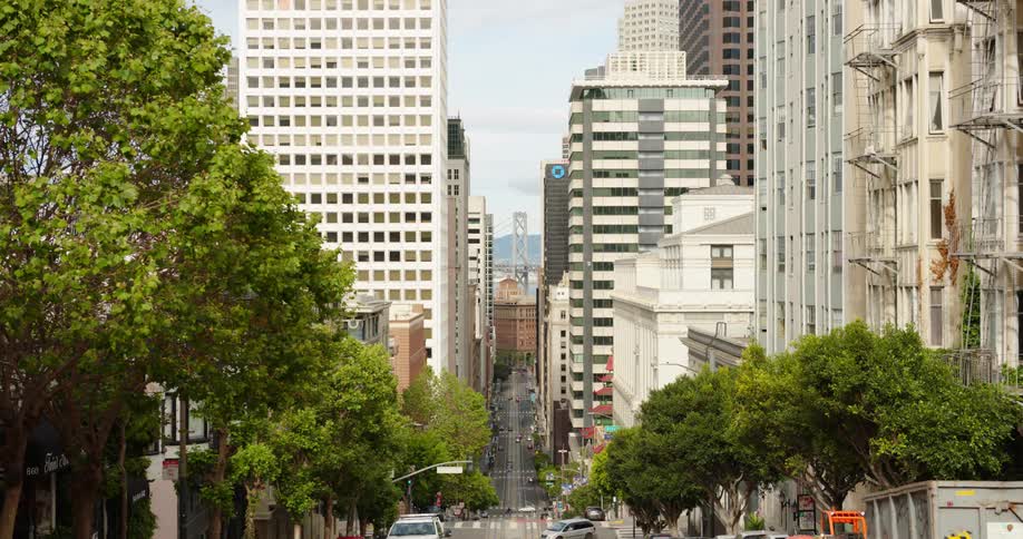 Light traffic on a wide street extending down a hill in a metropolis during the day