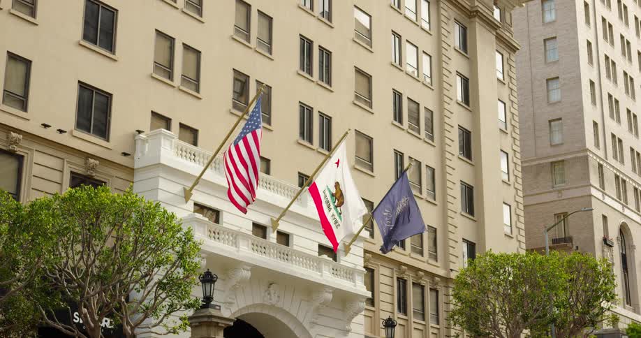 Flags representing the united states and california fly above the entrance to a large building