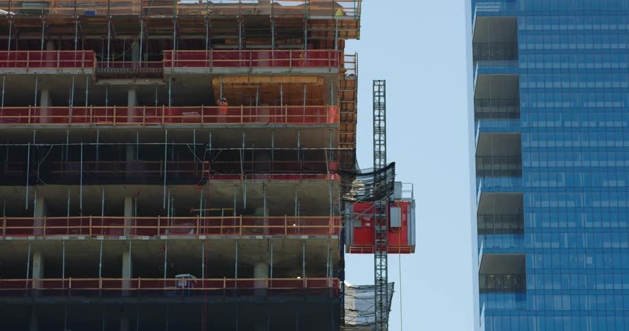 A construction worker with a hard hat and vest standing in an unfinished building with the sky in the background