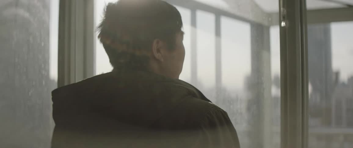 Person stands looking out of a window at a city