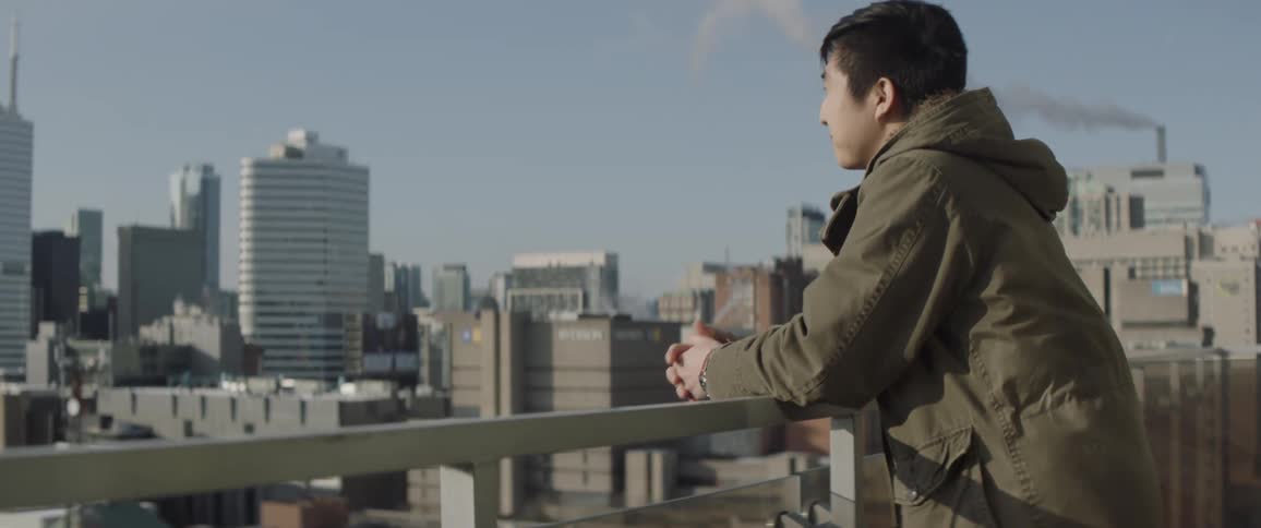 A man leans over the balcony overlooking the city and smiles