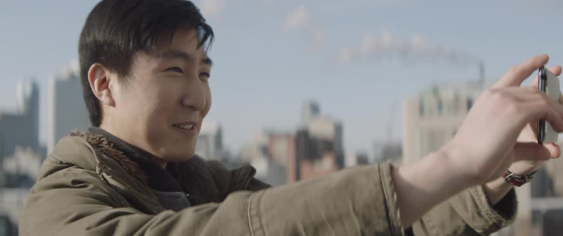A man pulls out his phone to take a selfie by the view of a city