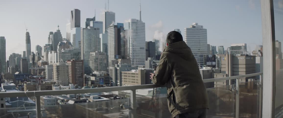 Man leans on a balcony railing looking out at the city