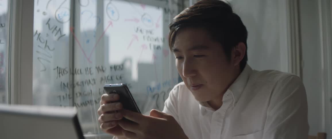 A man holds a mug and looks out the window before picking up his phone