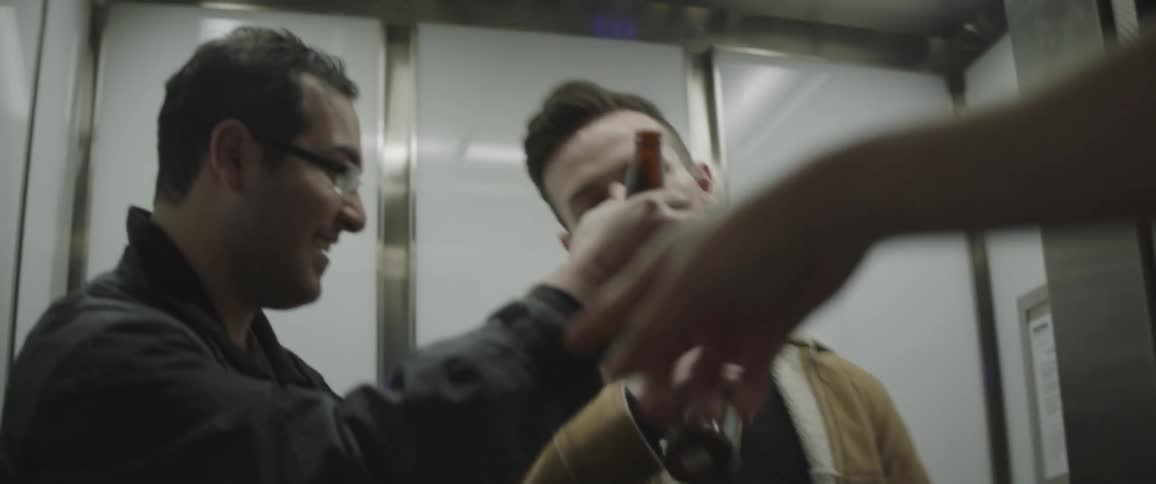 A man says goodbye to friends in an elevator by toasting with beer bottles