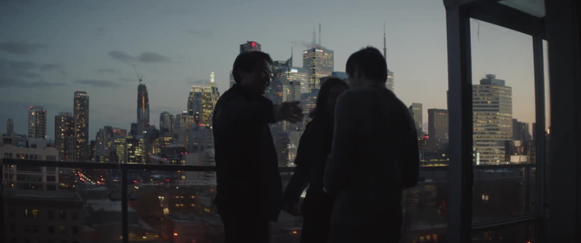 A man greets two people standing on a balcony overlooking a city