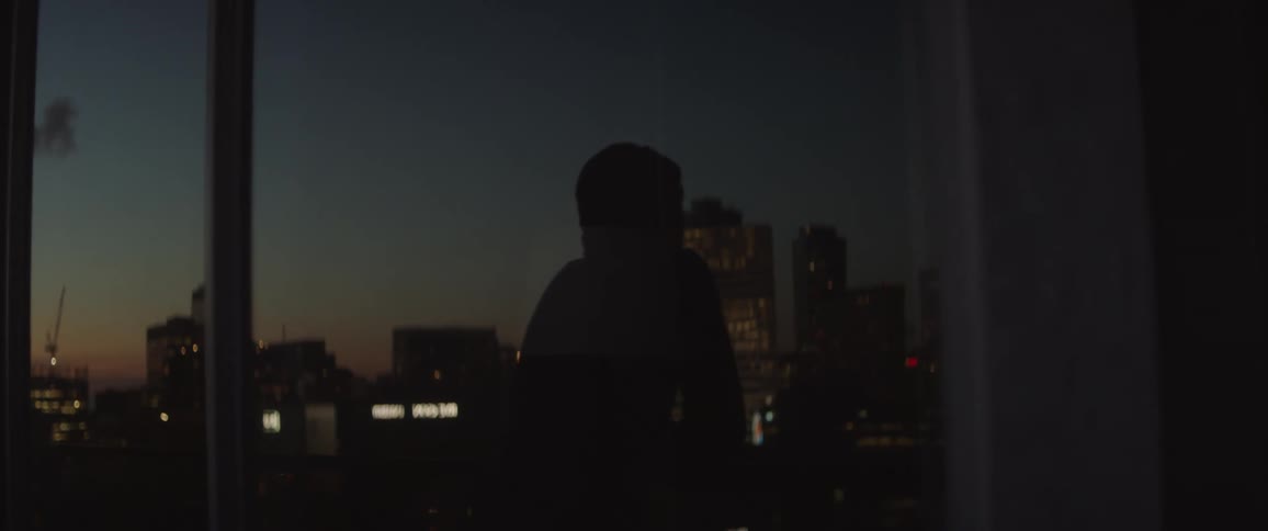 Silhouette of a person standing outside on a balcony looking at the city