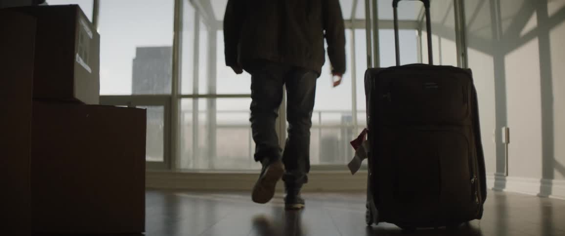 A man drags his luggage over to the window and looks outside