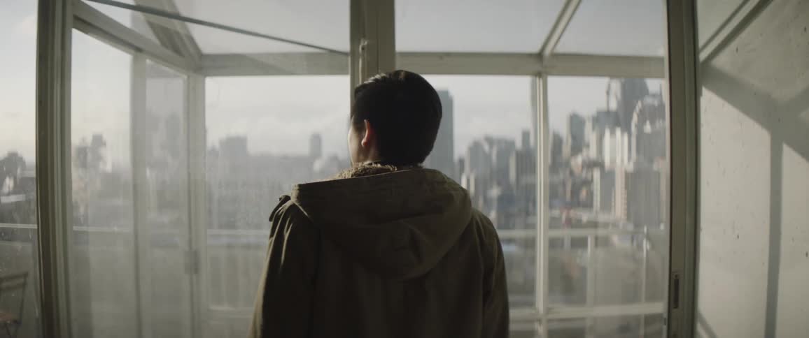 A man walks over to the window overlooking the city
