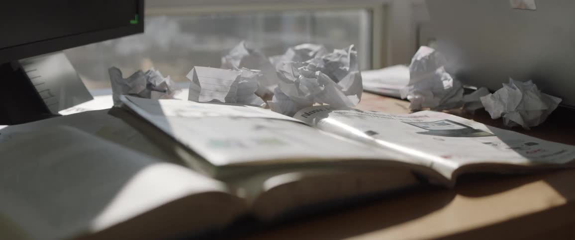 Open books and crumpled papers sit on a desk near a window