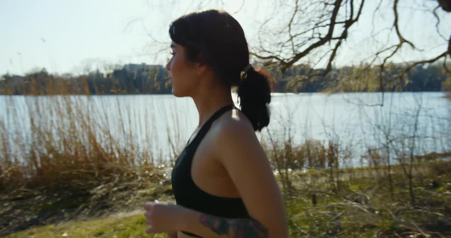 Young woman runs on wooded trail near lake