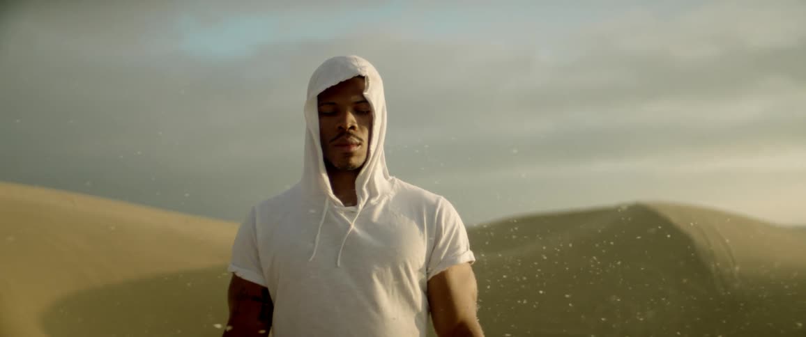 A man stands in a desert as sand particles blow around him